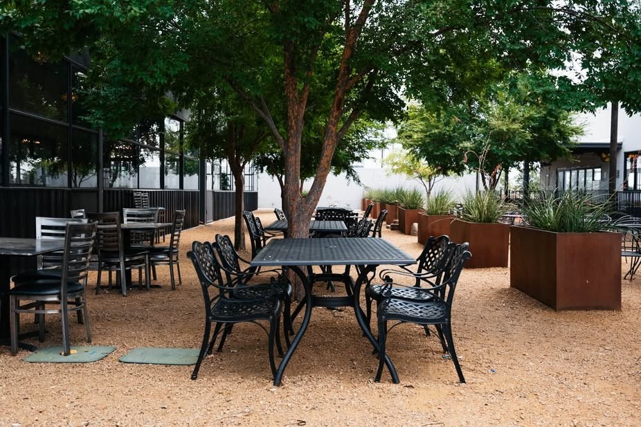 Open-air courtyard oasis with shaded seating under trees at Twisted Bar and Grill